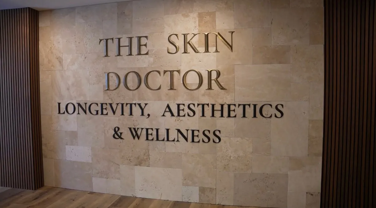 Engraved travertine feature wall reading “The Skin Doctor — Longevity, Aesthetics & Wellness”