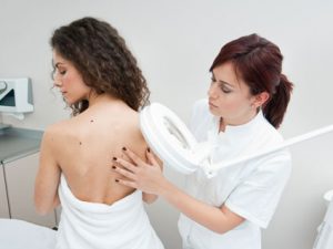 Dermatologist doctor inspecting woman skin for moles and melanoma